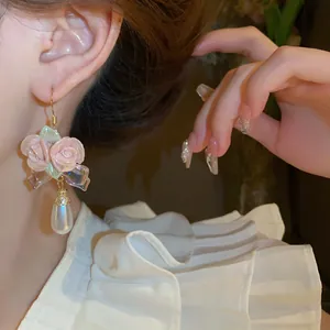 Detail view showing ceramic pink rose and teardrop pearl earrings worn on a model
