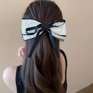 Detail view of large white lace bow hair clip with black ribbon on brown wavy hair