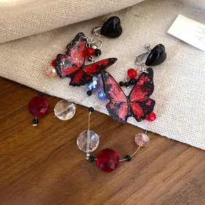 Close-up of red and black butterfly earrings with sparkling bead tassels on linen