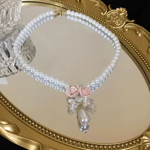 Elegant pearl necklace with pink ceramic roses and a teardrop pearl pendant on a gold tray.