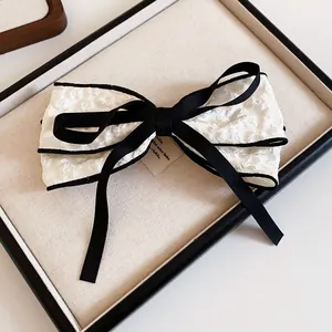 Close-up of white textured fabric bow hair clip with black ribbon accent details