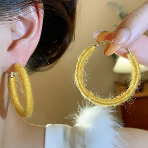 Close-up detail of stylish yellow fabric-wrapped woven hoop earrings for autumn and winter.