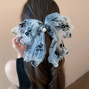 Detail view of elegant white lace bow hair clip with black floral embroidery and pearl.