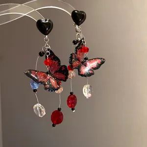 Detailed close-up of red and black butterfly earrings with glitter accents and bead tassels.