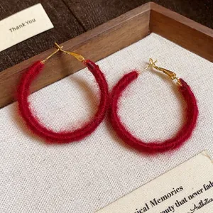 Detailed macro view of red fabric woven hoop earrings with golden clasps on warm fabric.