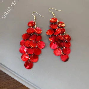 Detailed macro view of red shell tassel dangle earrings on a minimalist grey book cover.