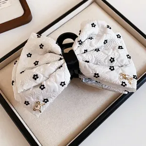 Detailed view of an elegant white fabric bow hair claw clip featuring black floral prints