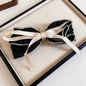 Elegant black fabric bow hair clip with cream ribbon detail on display tray