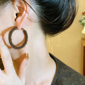 Close-up detail of brown fabric woven circular hoop earrings showing soft winter texture