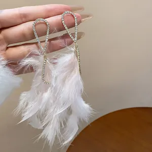 Dettaglio di eleganti orecchini con strass e nappe in piume bianche e morbide per donna.