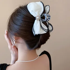 Elegant white fabric bow hair claw clip with pearl embellishment shown on model hair