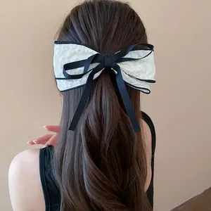 Elegant white fabric bow hair clip with black ribbon detail shown on model's hair