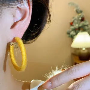 Detailed view of yellow fabric-wrapped woven hoop earring worn by a model in warm setting