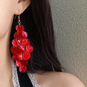 Close-up detail showing vibrant red tiered round shell tassel earrings on a model