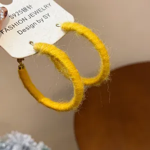 Close-up view of yellow fabric woven hoop earrings with S925 silver needles on a white card