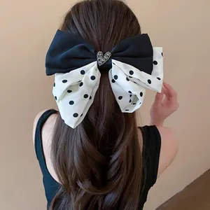 Detail view of a large black and white polka dot bow hair clip with a sparkly heart center