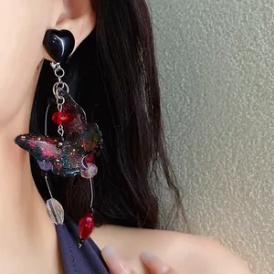 Detailed view of a colorful butterfly drop earring with heart stud and red beads