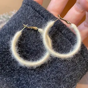 Close-up of white fuzzy yarn-wrapped hoop earrings with golden finish metal hooks