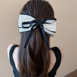 Elegant oversized white lace bow hair clip with black ribbon accent shown on long hair