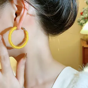 Close-up of a model wearing yellow fabric-wrapped minimalist hoop earrings for winter