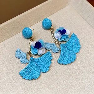 Holiday style raffia ginkgo leaf earrings with blue fabric flower accents on beige background
