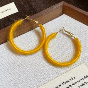 Detailed macro view of yellow yarn-wrapped hoop earrings on textured wooden display tray