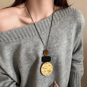 Minimalist geometric resin pendant necklace with leather cord on a grey sweater.