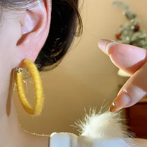 Close-up detail of a minimalist yellow fabric woven hoop earring for a cozy winter look