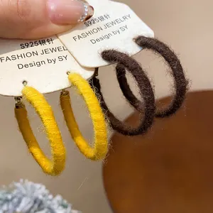 Close-up detail of textured fabric woven hoop earrings in yellow and dark brown colors