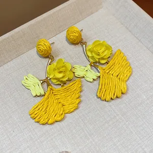 Close-up of yellow raffia ginkgo leaf earrings with delicate fabric rose accents.