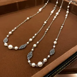 Detail view of a long vintage faux pearl necklace featuring delicate silver flower links.