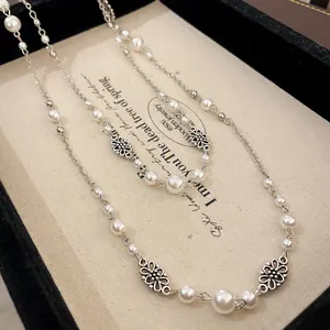 Detailed view of vintage flower charms and white faux pearls on a long silver necklace.