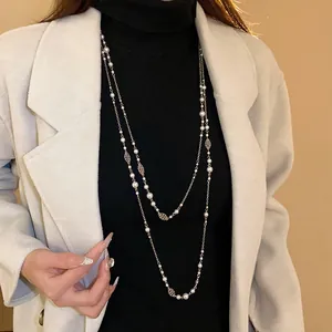 Elegant long layered pearl necklace with flower charms worn over a black sweater