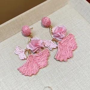 Close-up of pink raffia woven ginkgo leaf earrings with fabric flower accents.