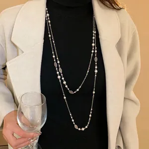 Elegant French retro long necklace with flowers and pearls draped over a black sweater