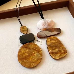Close-up of geometric resin pendants with marble texture on black cord necklace