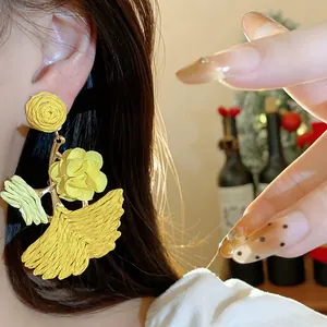 Close-up of yellow raffia woven ginkgo leaf earrings on model for resort style.