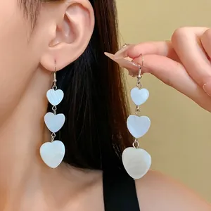 Elegant triple heart drop earrings featuring iridescent shell-like finish shown on a model