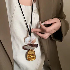 Detail showing a vintage geometric resin pendant necklace styled on a brown blazer.