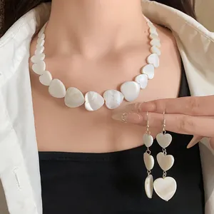 Detail showing irregular white heart-shaped shell necklace and matching drop earrings on model