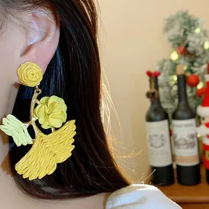 Close-up detail of vacation style yellow raffia ginkgo leaf drop earrings worn by a model.