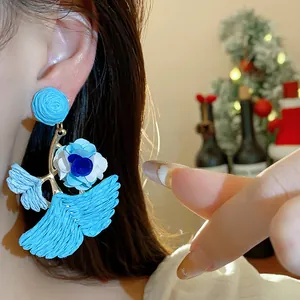 Detailed macro shot of blue raffia ginkgo leaf and floral drop earrings on a model
