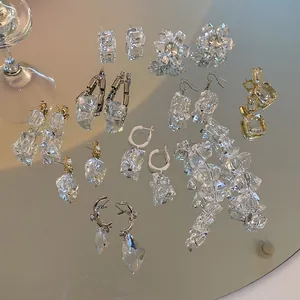 Detail view of transparent irregular ice cube earrings displayed on a mirror surface.