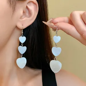 Close-up detail of elegant white tiered heart drop earrings on an Asian model's ear