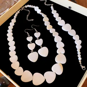 Elegant white shell heart-shaped necklace, earrings, and bracelet jewelry set on black velvet.