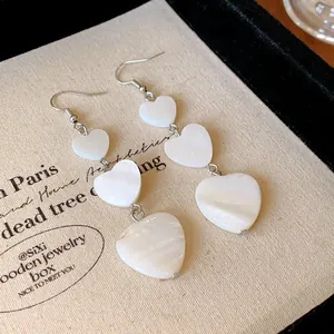 Elegant white heart-shaped tiered dangle earrings with pearl luster shell texture.