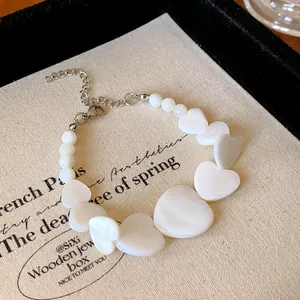 Elegant necklace featuring white heart-shaped shell beads and silver chain on fabric