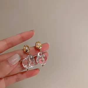 Close-up view of irregular transparent ice-block earrings with gold-tone pearl studs.