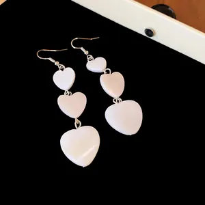 Detailed view of white triple heart drop earrings on black velvet tray