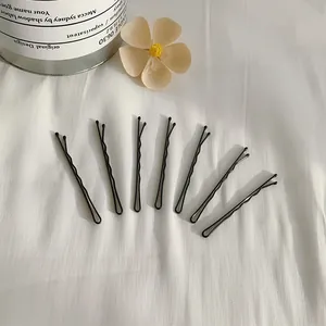 Elegante set di 7 forcine nere opache minimaliste disposte su sfondo di tessuto bianco